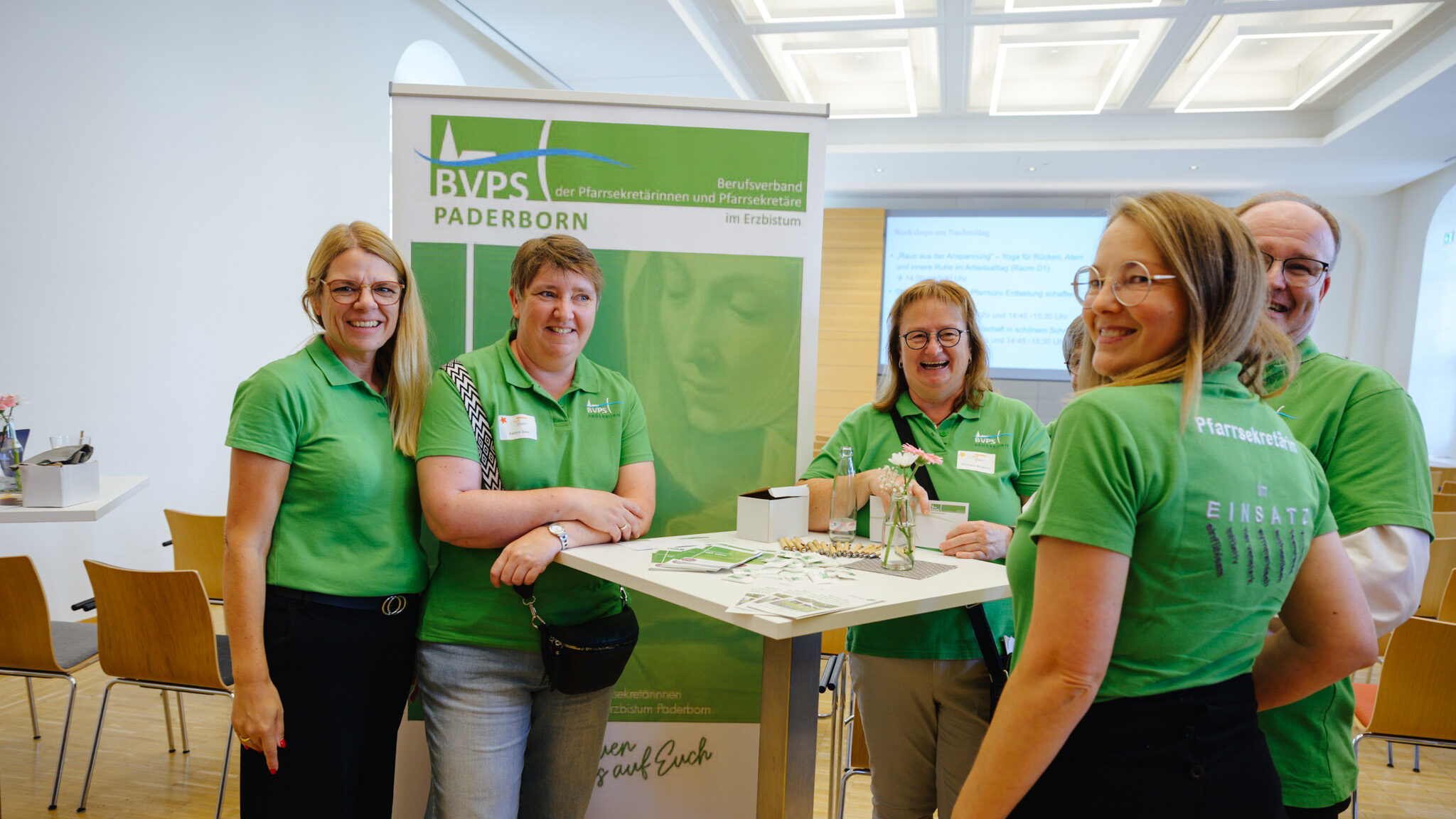 Vier Damen in grünem T-shirt, die an einem Stehtisch stehen. Im Hintergrund ist ein grünes Roll-up